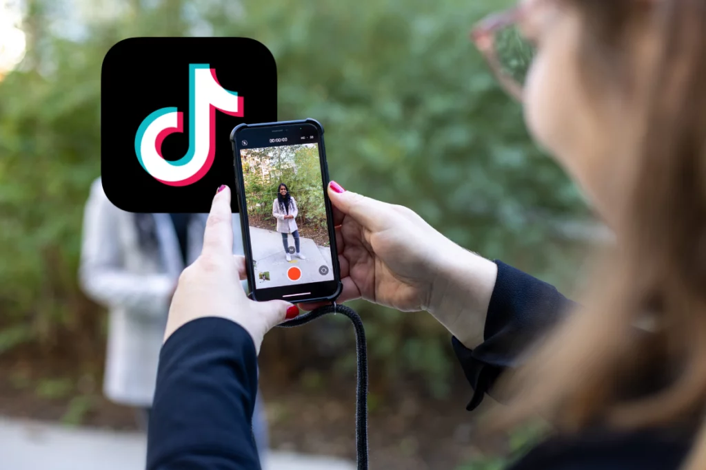 Person filmt mit einem Smartphone eine weitere Person; TikTok-Logo im Vordergrund