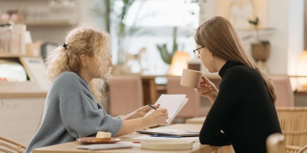 Two women are discussing notes at a table