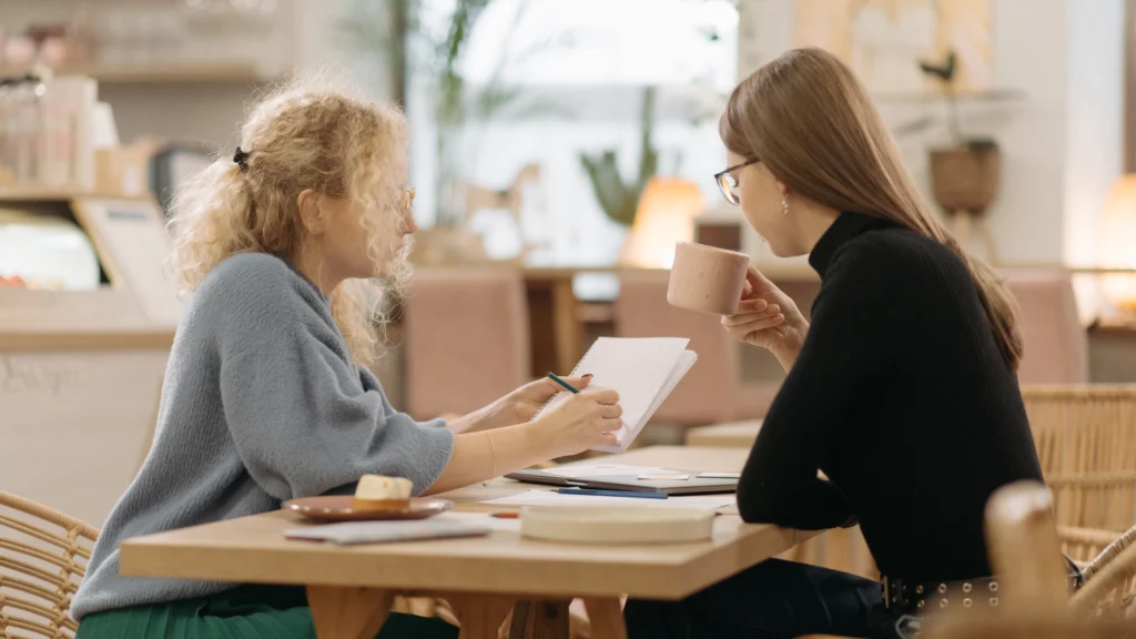 Two women are discussing notes at a table