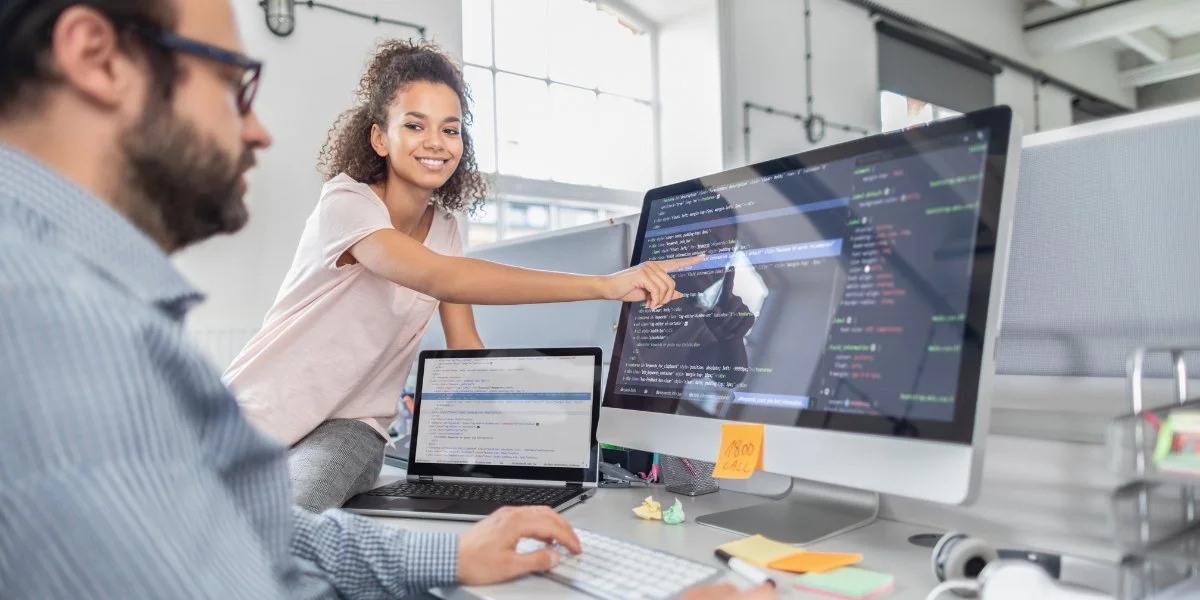 Two people are working on software code on multiple screens