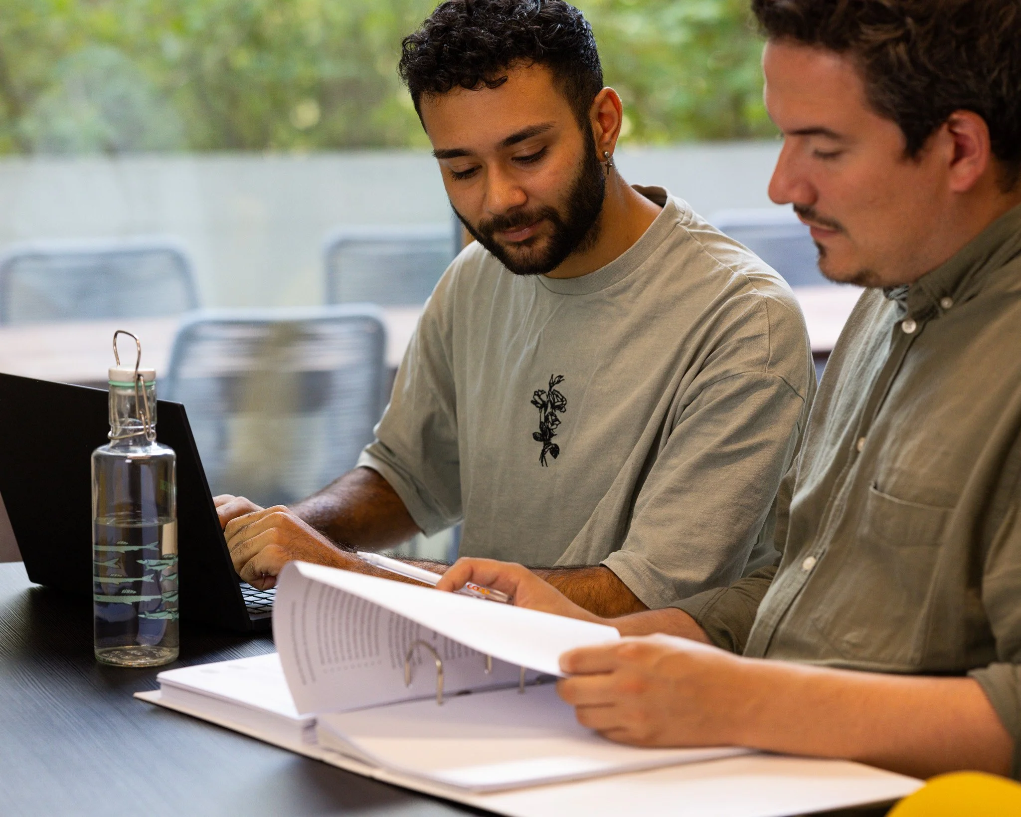 Two employees are working together using a laptop and documents