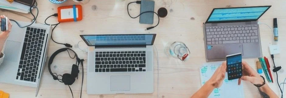A bird's-eye view of a workspace with three laptops and a smartphone