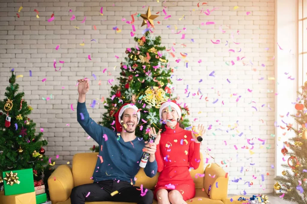 A couple celebrates with confetti in front of a decorated Christmas tree