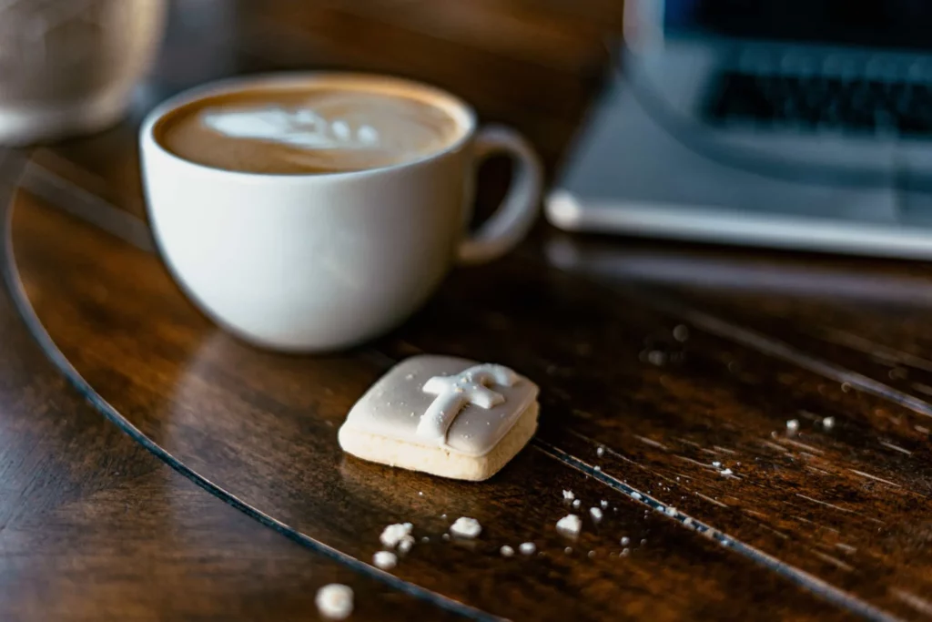 Kaffeetasse, Laptop und Keks mit Facebook-Logo auf einem Holztisch.