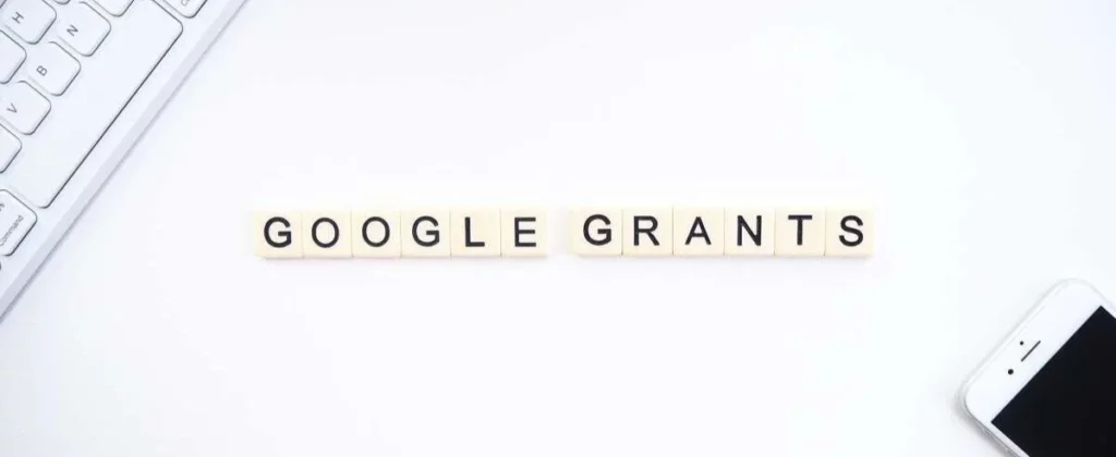 "Google Grants" lettering on letter tiles next to a keyboard and smartphone