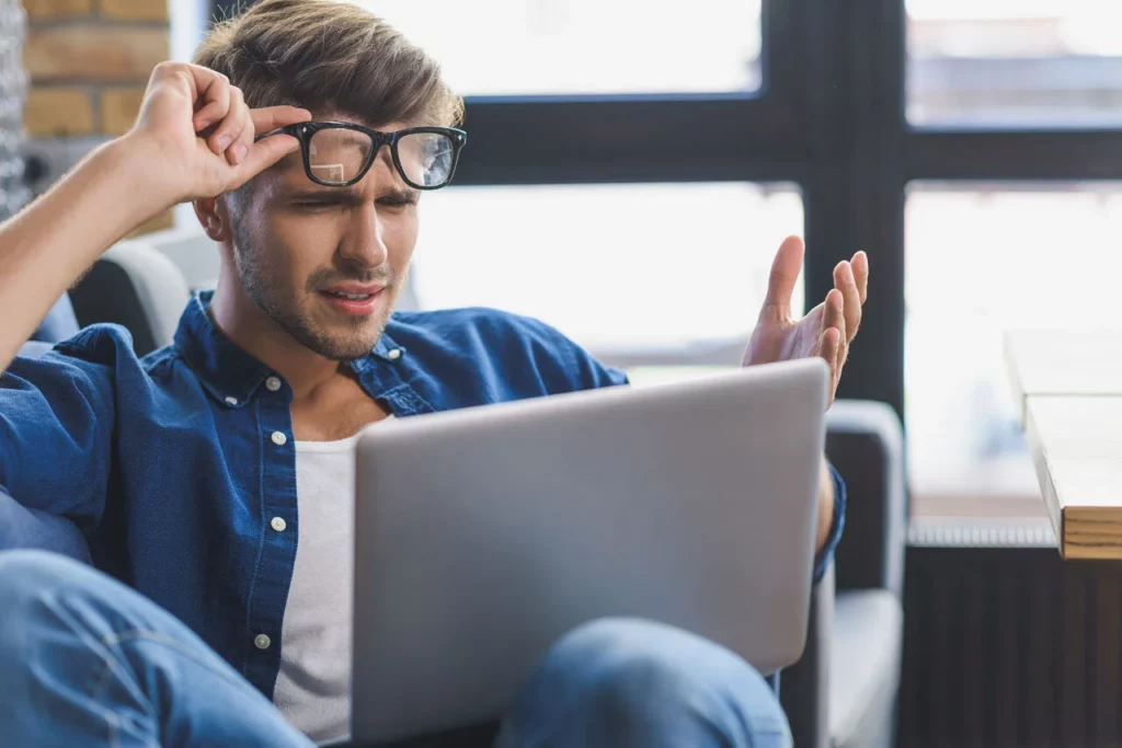 Mann blickt irritiert auf einen Laptop und hebt seine Brille