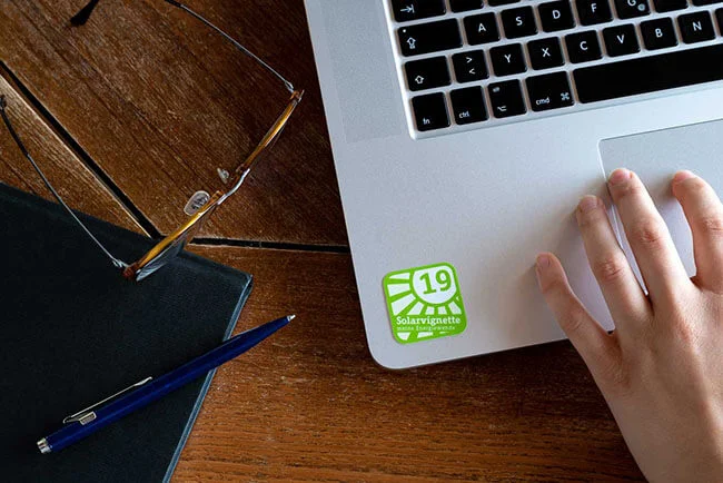 A hand operating a laptop with a green solar sticker from 2019