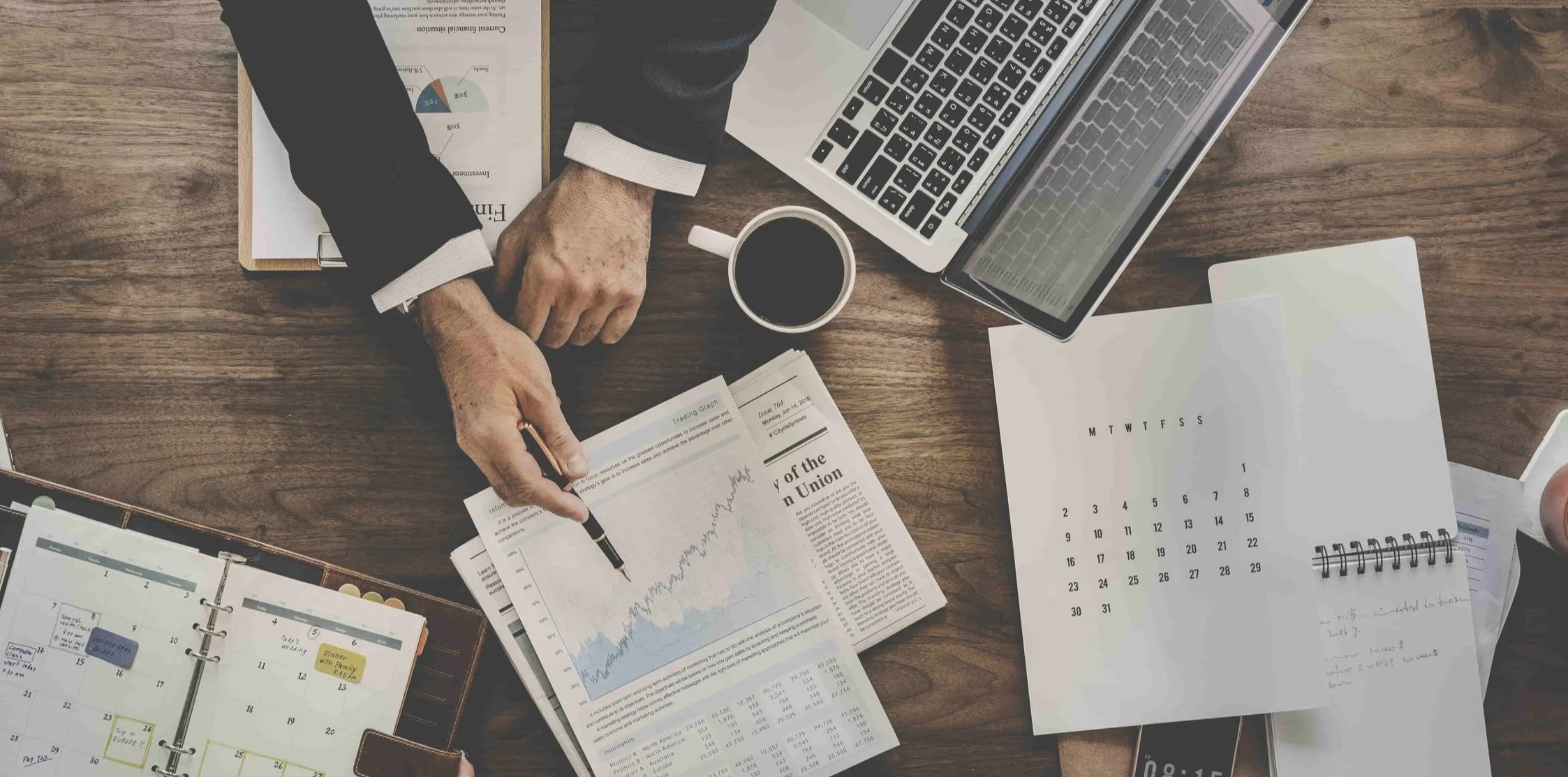 Data Analysis at a Desk with a Laptop, Charts, and a Calendar