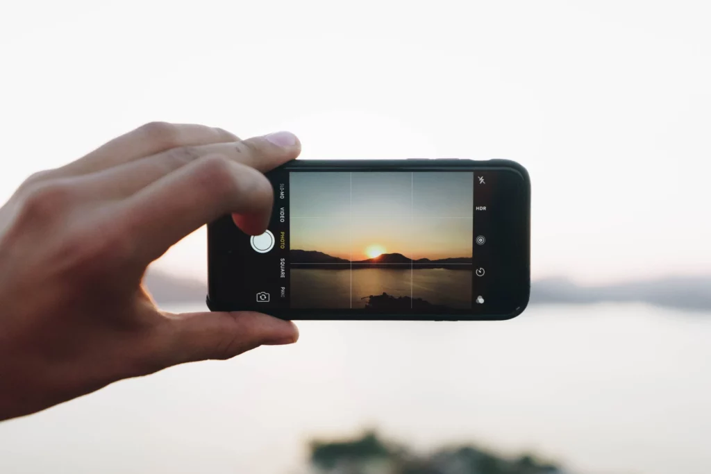 A hand is taking a picture of a sunset with a smartphone.