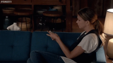 Une femme est assise sur un canapé et regarde son smartphone.