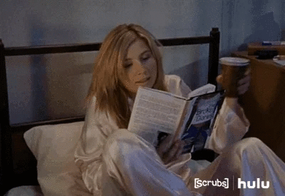 Une femme lit un livre, l'air détendu, un gobelet à la main.