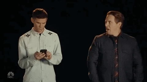 Deux hommes se tiennent côte à côte ; l'un d'eux regarde son smartphone.