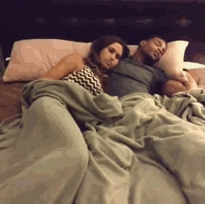 Two people are lying in bed, while a smartphone has their attention.