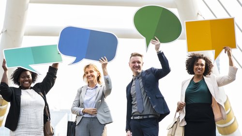 Four people are holding up signs with colored speech bubbles.