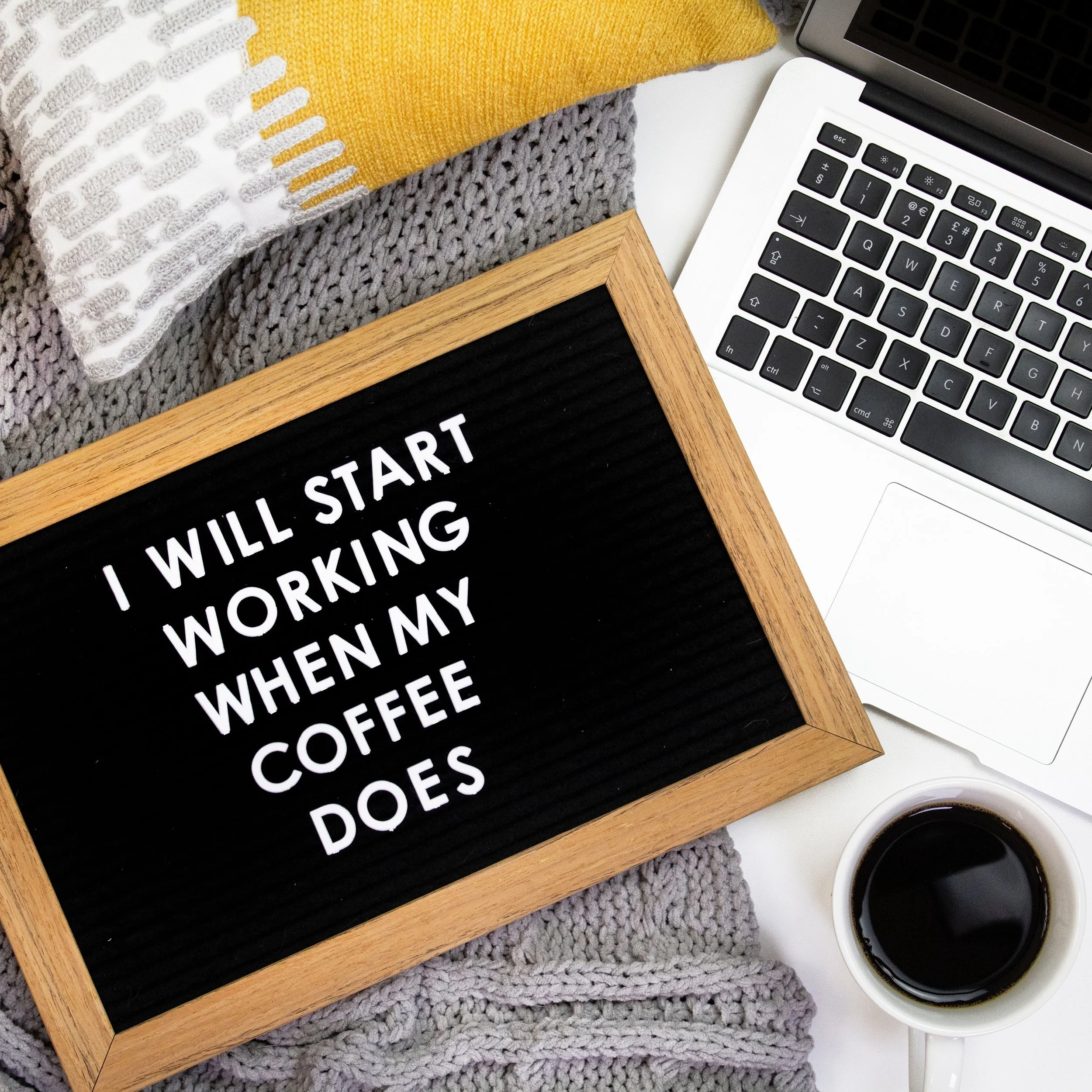 Workstation with a laptop, coffee, and a chalkboard with an English saying