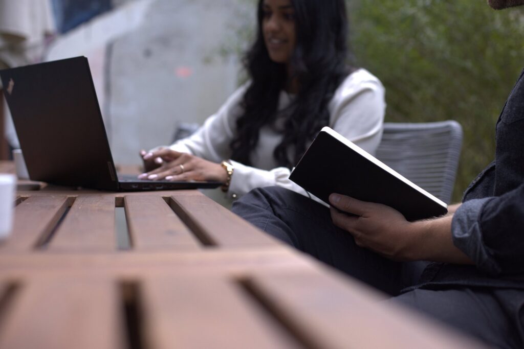 Zwei Personen arbeiten draussen an einem Tisch mit Laptop und Notizbuch
