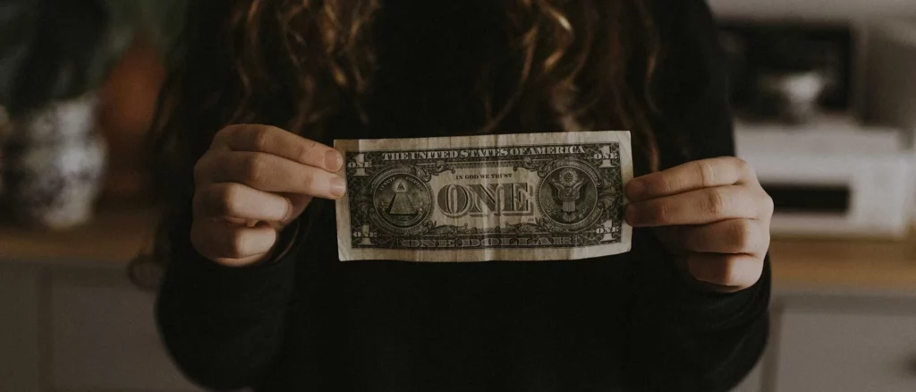 A person is holding a one-dollar bill in front of them
