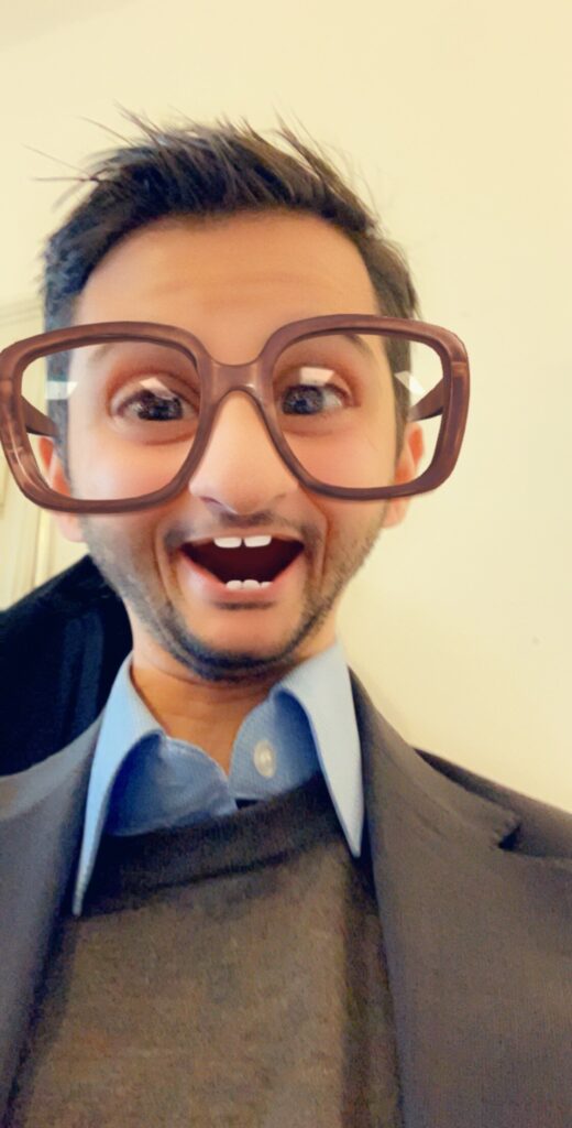 Man in a suit with a Snapchat filter featuring oversized glasses and eyes