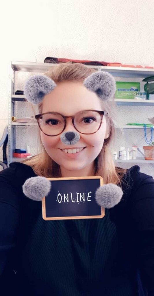 A woman wearing a Snapchat filter with bear ears and a bear nose is holding a sign that says "ONLINE"