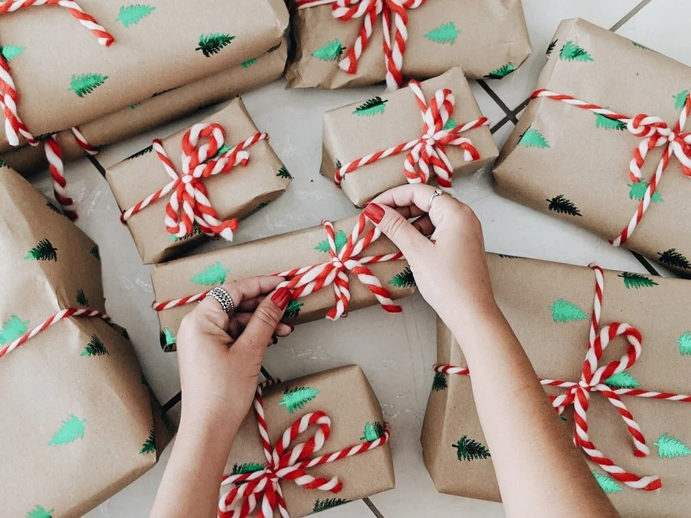 Des mains nouent un cordon rouge et blanc autour de cadeaux de Noël emballés dans du papier d'emballage